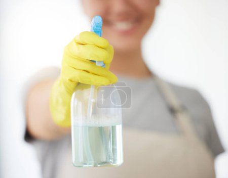Foto de One unrecognizable woman holding a cleaning product while cleaning her apartment. An unknown domestic cleaner wearing latex cleaning gloves. - Imagen libre de derechos