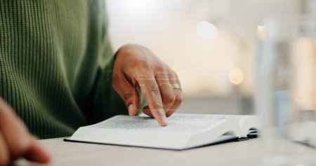Photo for Closeup hand, reading and a bible for faith, spiritual support or hope from scripture. House, table and a person with a book for worship, trust or education on God, Jesus or learning about religion. - Royalty Free Image