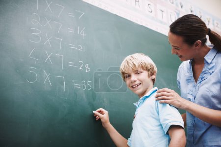 Photo for Shes always there to help. A pretty teacher standing at the blackboard with a young student and helping him with his maths - Royalty Free Image