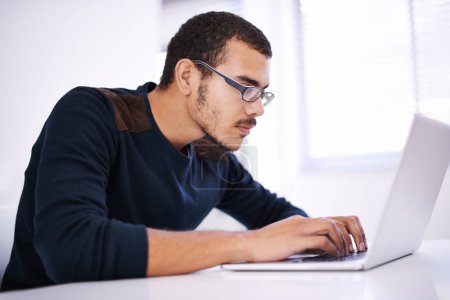 Téléchargez les photos : Traversant facilement les lignes de code. un beau jeune homme travaillant sur son ordinateur portable dans un bureau - en image libre de droit