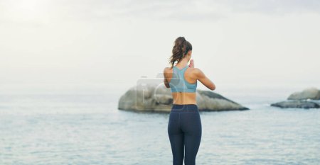 Photo for Listening to the waves soothes my restless soul. Rearview shot of an unrecognizable woman standing and doing yoga alone by the ocean during an overcast day - Royalty Free Image