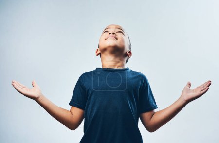 Foto de Gracias a Dios por todo. Estudio de un niño lindo abriendo los brazos y mirando hacia arriba sobre un fondo gris - Imagen libre de derechos
