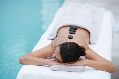 Téléchargez les photos : La thérapie aux pierres chaudes l'enlève ses soucis. une belle femme allongée sur une table de massage au bord de la piscine - en image libre de droit