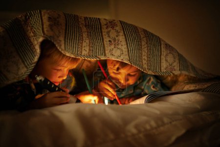 Photo for Bonding under their blankets. Two young brothers coloring in pictures while underneath their blanket after their bedtime - Royalty Free Image