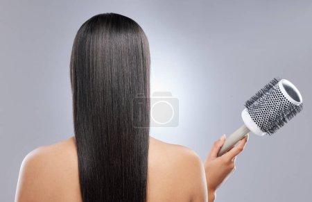 Photo for How to get sleeker than sleek hair. Rearview shot of a woman holding a blow-dry brush against a grey background - Royalty Free Image