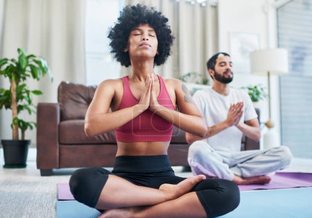 Téléchargez les photos : Le yoga fait partie de notre routine d'exercice hebdomadaire. un jeune couple pratiquant le yoga dans leur salon - en image libre de droit