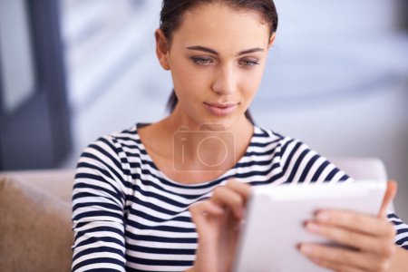 Foto de ¿Qué haría sin mi tableta? Una hermosa joven usando una tableta en su sofá - Imagen libre de derechos