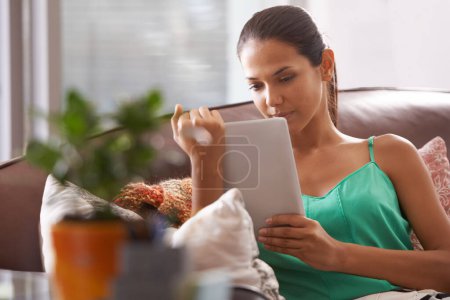 Foto de Este libro electrónico realmente la tenía agarrada. Una hermosa mujer sosteniendo su tableta digital mientras se relaja en su sofá - Imagen libre de derechos