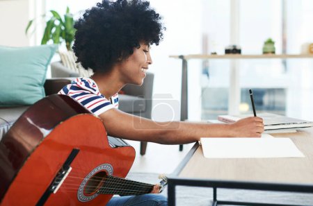 Téléchargez les photos : J'aime faire ma propre musique. une femme écrit dans son carnet tout en jouant de la guitare à la maison - en image libre de droit
