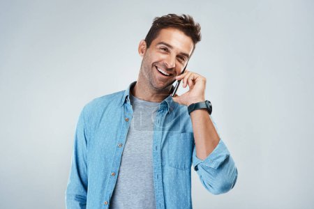 Photo for Yes this is him speaking. Studio shot of a cheerful young man talking on his cellphone while standing against a grey background - Royalty Free Image
