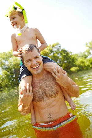 Foto de Acostado en el lago con papá. Joven padre en un lago llevando a su hijo sobre sus hombros mientras sonríe - Imagen libre de derechos