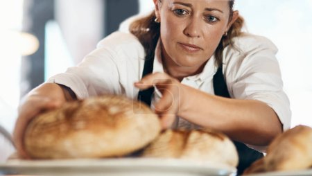 Téléchargez les photos : Du pain fraîchement cuit qui arrive. une femme mûre exposant une sélection de pains fraîchement cuits dans sa boulangerie - en image libre de droit