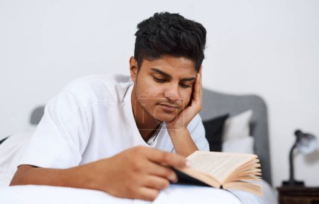 Téléchargez les photos : J'ai beaucoup lu dernièrement. un jeune homme lisant un livre allongé sur son lit - en image libre de droit