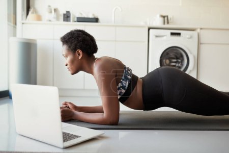 Téléchargez les photos : Planche ton chemin vers un ventre plus serré. une jeune femme utilisant un ordinateur portable pendant l'exercice à la maison - en image libre de droit