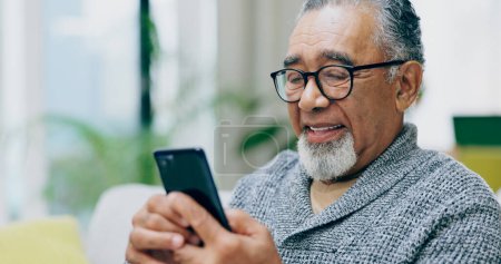 Photo for Senior man, smile and phone on sofa with texting, reading or click for contact in home living room. Elderly person, smartphone and happy for notification, social network app or relax on lounge couch. - Royalty Free Image