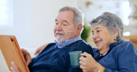 Photo for Tablet, tea and a senior couple in their home to relax together during retirement for happy bonding. Tech, smile or love with an elderly man and woman drinking coffee in their apartment living room. - Royalty Free Image