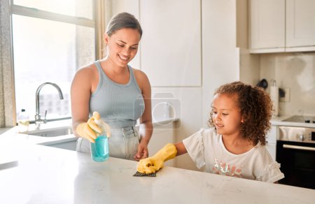 Photo for Little girl helping her mother with household chores at home. Happy mom and daughter wearing gloves while spraying and scrubbing the kitchen counter together. Kid learning to be responsible by doing . - Royalty Free Image