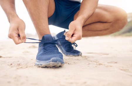 Photo for Tie them well to give your feet more support during your runs. Closeup shot of an unrecognisable man tying his laces while exercising on the beach - Royalty Free Image