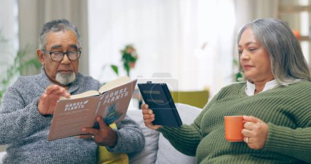 Photo for Reading, relax and senior couple on a sofa with book, tablet and coffee while bonding at home together. Literature, ebook and old people chilling with tea in a living room calm and enjoy retirement. - Royalty Free Image