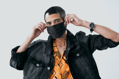 Photo for Who said face masks cant be fashionable. Studio shot of a young man putting on a face mask against a grey background - Royalty Free Image