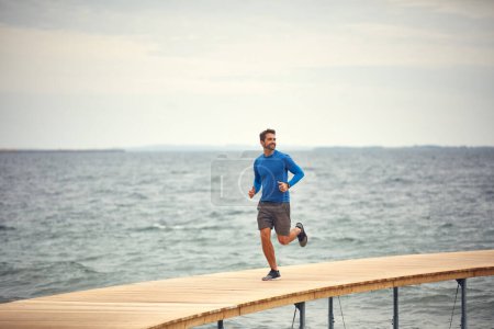 Téléchargez les photos : Commencez votre journée par une bonne course. un homme sportif d'âge moyen qui court au bord de la mer - en image libre de droit