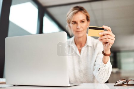 Téléchargez les photos : Maintenant, vous pouvez gérer votre argent 247. une femme d'affaires mature en utilisant un ordinateur portable et une carte de crédit dans un bureau - en image libre de droit