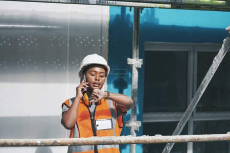 Photo for Staying on track with the days schedule. a young woman talking on a cellphone and checking the time while working at a construction site - Royalty Free Image