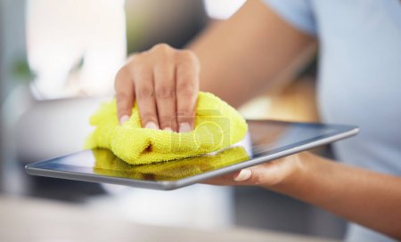 Photo for An unrecognizable woman cleaning her digital tablet in her apartment. One unknown woman using a rag to remove dust from her device. - Royalty Free Image