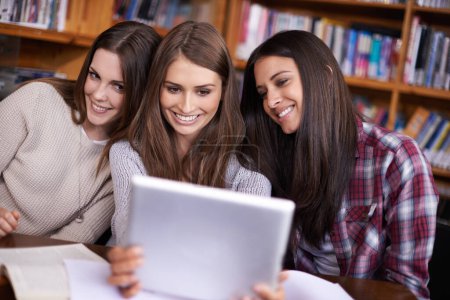 Foto de Serán mejores amigas para siempre. tres amigos sentados en la biblioteca tomando fotos de sí mismos con una tableta digital - Imagen libre de derechos