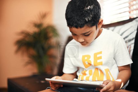 Téléchargez les photos : Devenir curieux du monde en ligne. un adorable petit garçon utilisant une tablette numérique sur le canapé à la maison - en image libre de droit