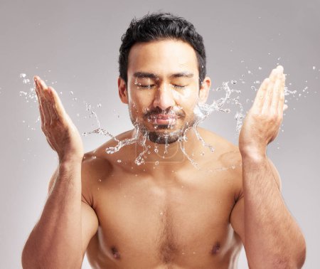 Photo for Handsome young mixed race man shirtless in studio isolated against a grey background. Hispanic male washing his face with water. Rinsing off his skin to keep it clean and hygienic as part of skincare. - Royalty Free Image