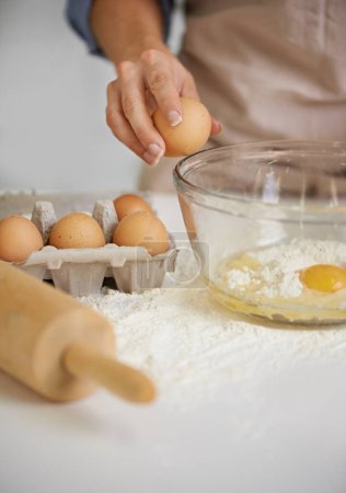 Foto de Para hacer un pastel tienes que romper unos huevos. Primer plano de una mujer poniendo ingredientes en un tazón en su cocina - Imagen libre de derechos