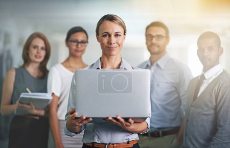 Photo for The secret to business success. Portrait of a businesswoman holding a laptop with her colleagues blurred in the background - Royalty Free Image