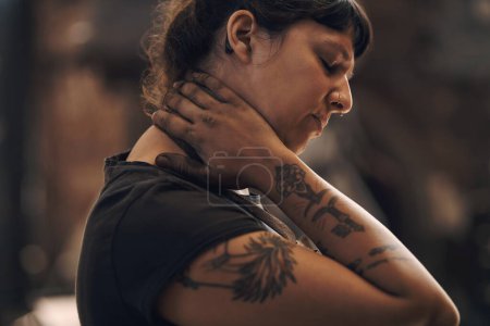 Foto de Levantamiento pesado hace un número en sus ligamentos. una mujer joven que experimenta dolor de cuello mientras trabaja en una fundición - Imagen libre de derechos