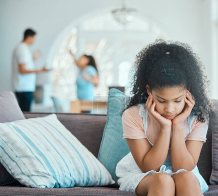 Foto de Cómo hacer que su hija resienta. una niña que se ve triste en un sofá mientras sus padres discuten en el fondo - Imagen libre de derechos