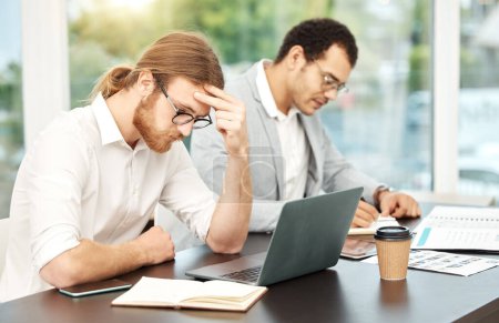 Photo for I just cant focus today. a young businessman looking stressed out while working on a laptop in an office with his colleague in the background - Royalty Free Image