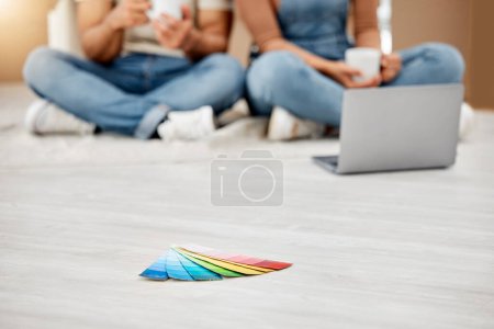 Foto de Todo se trata de color. Primer plano de muestras de color en el suelo con una pareja irreconocible usando una computadora portátil en el fondo mientras se muda de casa - Imagen libre de derechos