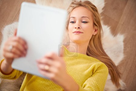 Foto de Su libro electrónico se estaba poniendo intenso. Una joven tirada en el suelo leyendo un libro en su tableta digital - Imagen libre de derechos