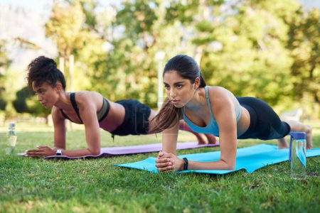 Photo for Hold it Hold it. Full length shot of two attractive young women holding a plank position in the park during the day - Royalty Free Image