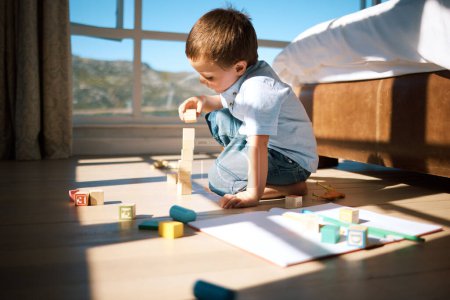 Photo for Little boy building a tower with wooden blocks. Adorable caucasian child stacking toys while developing fine motor skills and hand-eye coordination. Boy playing with building blocks or wooden cubes. - Royalty Free Image