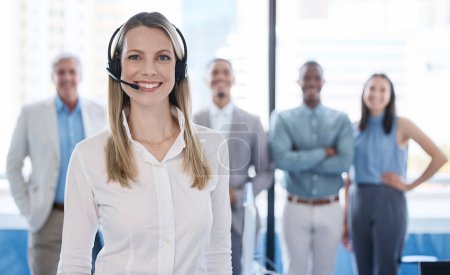Photo for Lets make life a lot easier for you. Portrait of a mature businesswoman using a headset in a modern office with her team in the background - Royalty Free Image