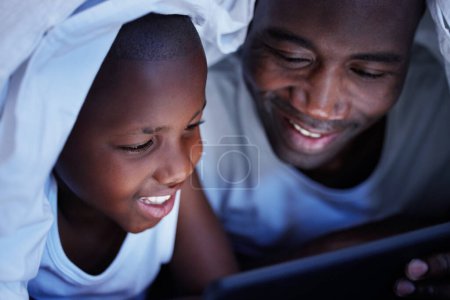 Foto de La familia es lo más importante del mundo. un padre y un hijo usando una tableta en la cama por la noche - Imagen libre de derechos