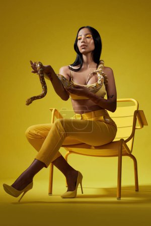 Photo for Just follow the yellow. a fashionable woman holding a snake while modelling a yellow concept - Royalty Free Image