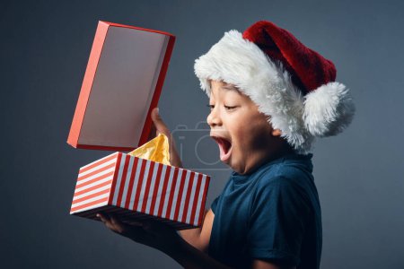 Foto de Hay un Santa. Estudio de un niño lindo abriendo un regalo de Navidad sobre un fondo gris - Imagen libre de derechos