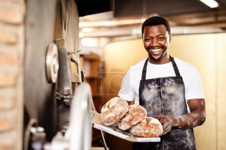 Foto de Ahora todo lo que necesitas es mantequilla. un panadero macho sosteniendo pan recién horneado en su panadería - Imagen libre de derechos