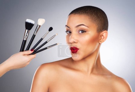 Photo for Theres a wand for every kind of magic. Studio shot of a hand holding makeup brushes next to a beautiful young womans face - Royalty Free Image