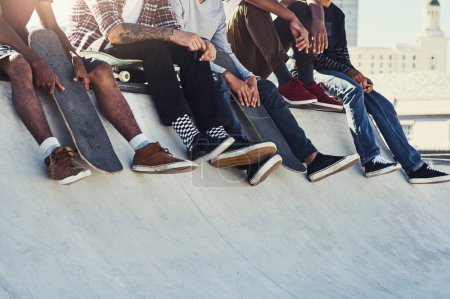 Foto de Dando patadas en el skatepark. un grupo de patinadores irreconocibles sentados juntos en una rampa en un skatepark - Imagen libre de derechos