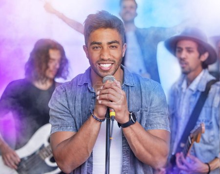Photo for Theyre a group of crowd pleasers. Cropped portrait of a handsome young male singer performing on stage with his bandmates in the background - Royalty Free Image