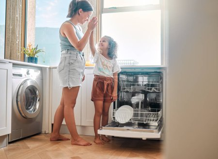 Photo for Little girl helping her mother with household chores at home. Happy mom and daughter giving high five while unloading the dishwasher together. Kid learning to be responsible by doing tasks. - Royalty Free Image