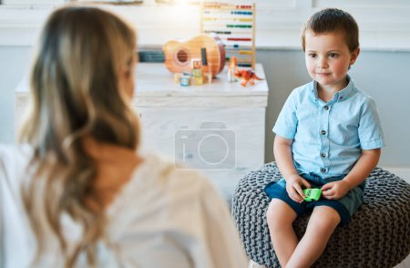 Photo for An adorable little boy sitting in his bedroom at home and talking to his mother. Happy male child bonding with his mom. Rearview of a blonde woman spending quality time with her young son on a weeken. - Royalty Free Image